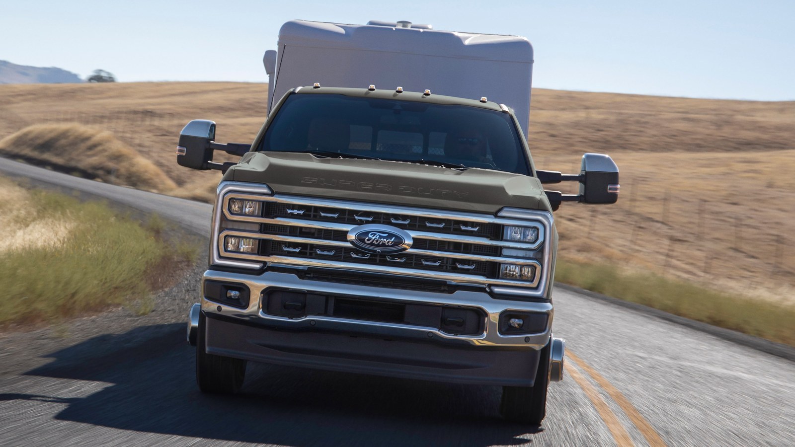 2026 Ford Super Duty dual-rear-wheel pickup towing a camper on a rural road