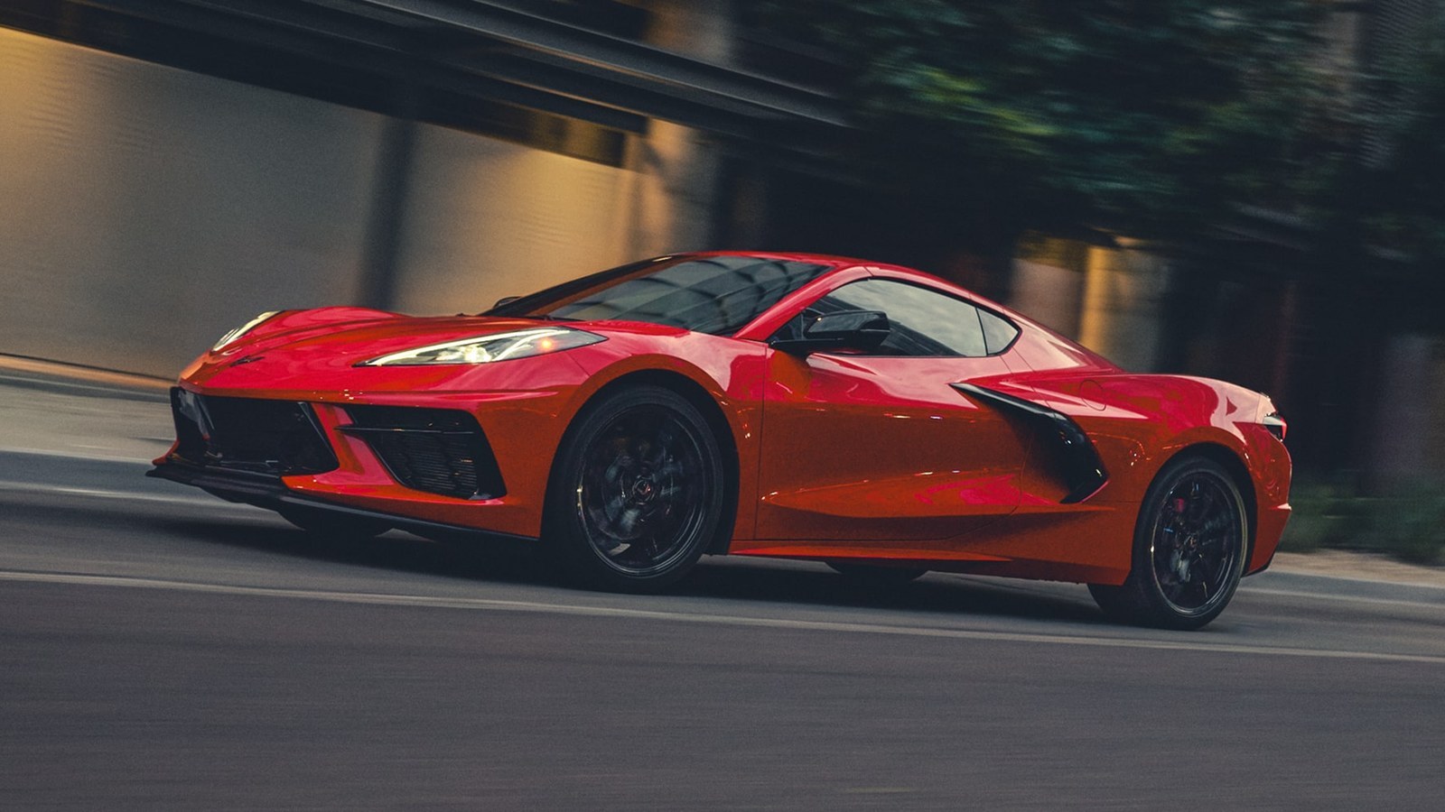 Red 2027 Chevrolet Corvette Stingray coupe driving on a city street, front three-quarter view