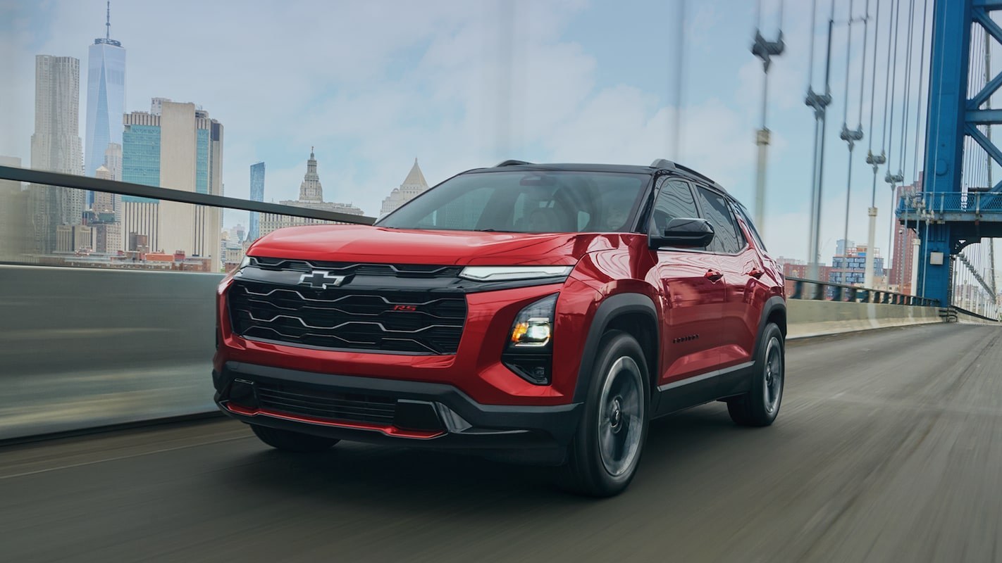 Red 2027 Chevrolet Equinox RS driving across a bridge with a city skyline behind it