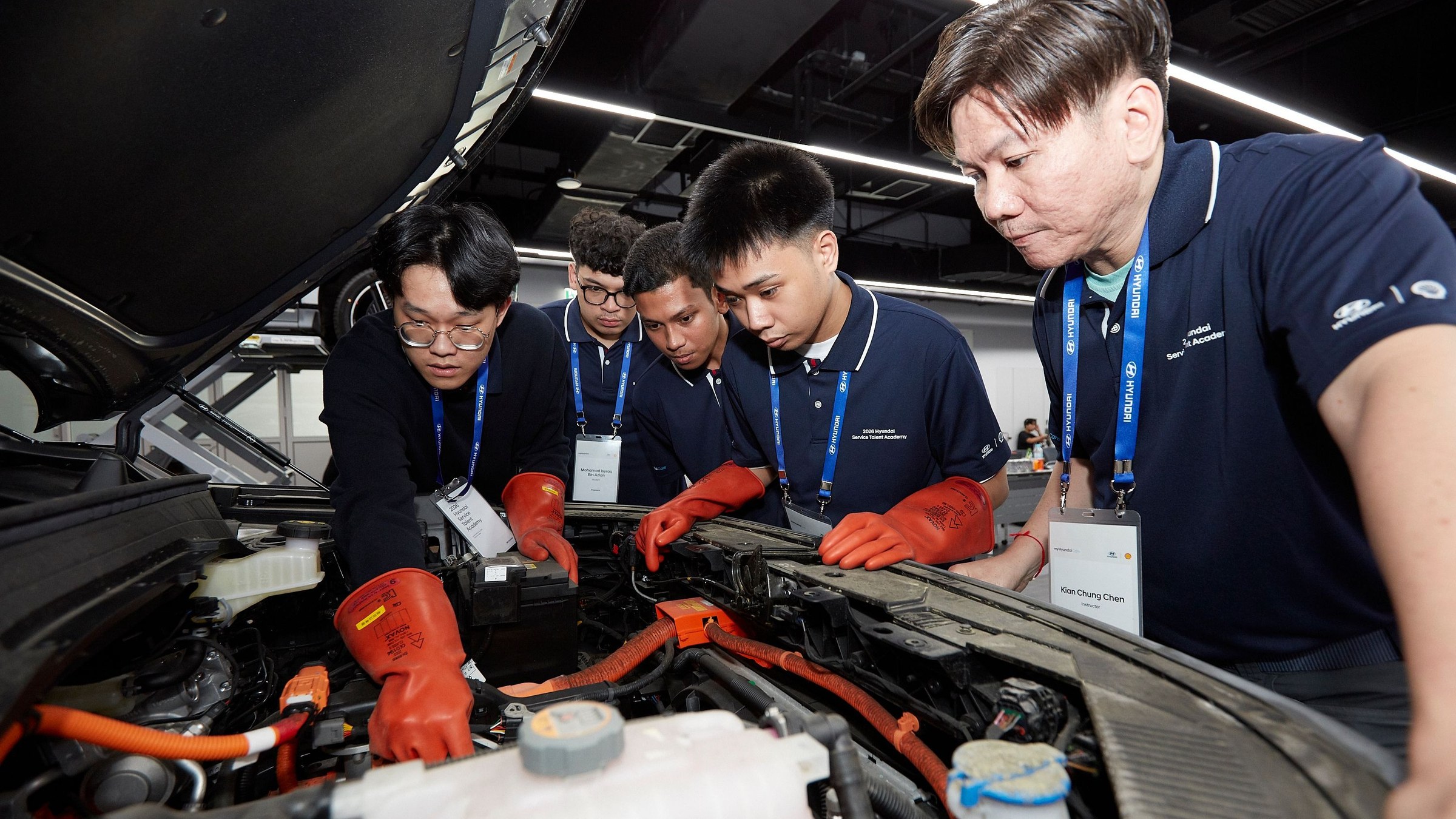 Service trainees in high-voltage safety gloves work on a hybrid engine bay at a Hyundai training center
