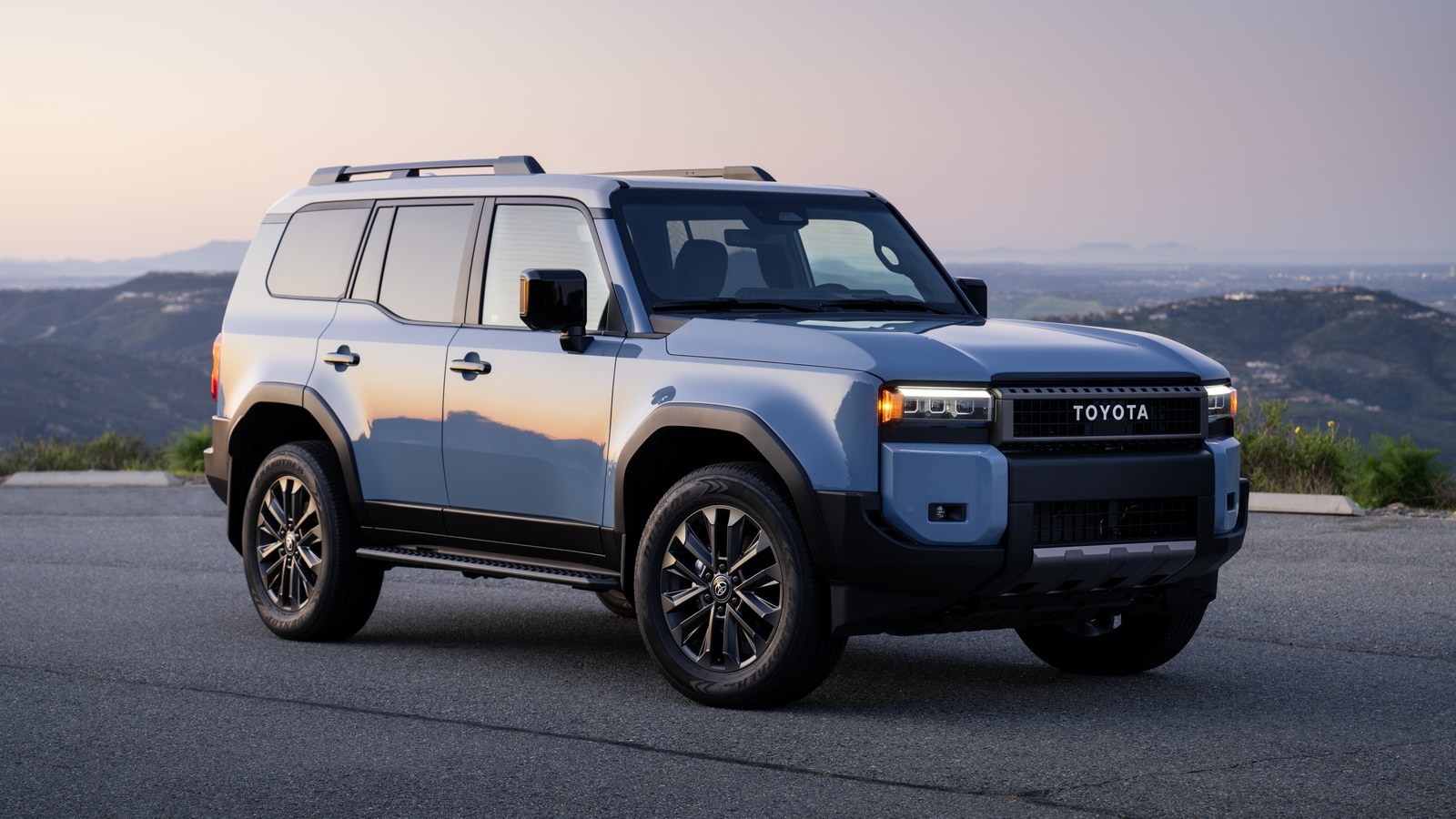 Blue Toyota Land Cruiser parked on a mountain overlook at dusk, front three-quarter view