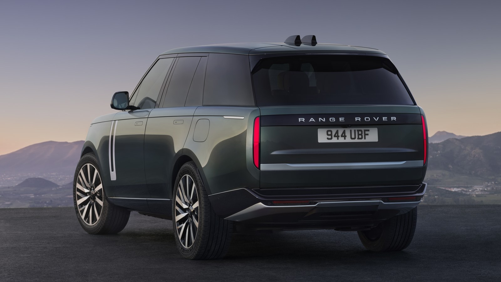 Dark green current-generation Range Rover seen from the rear three-quarter angle, tailgate in view, at dusk