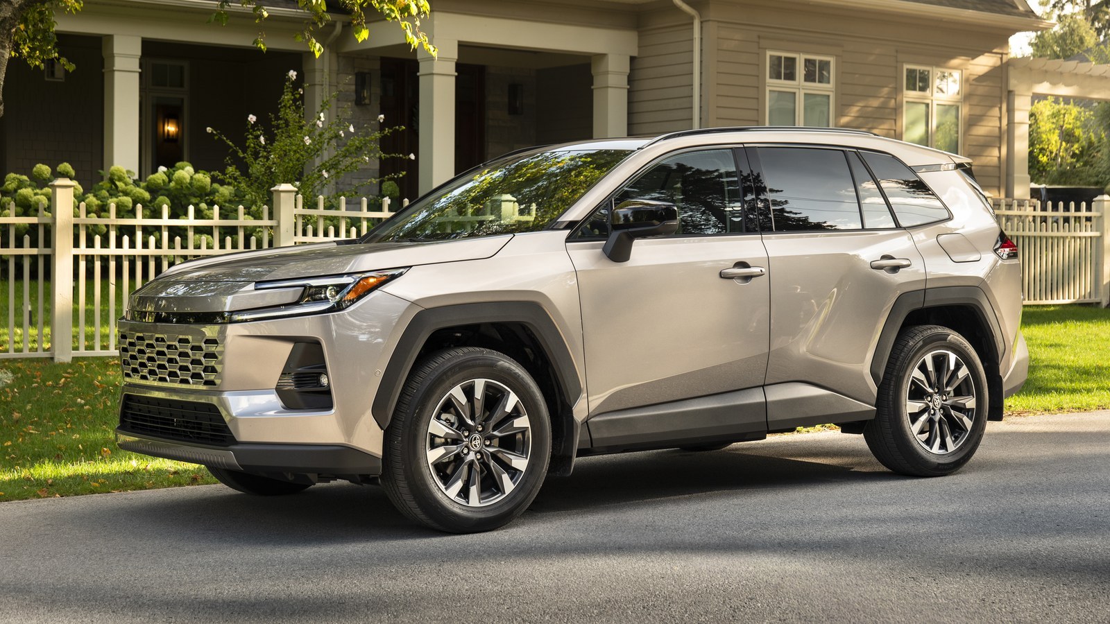 2026 Toyota RAV4 Limited Hybrid in a silver-beige finish parked in front of a house with a white picket fence