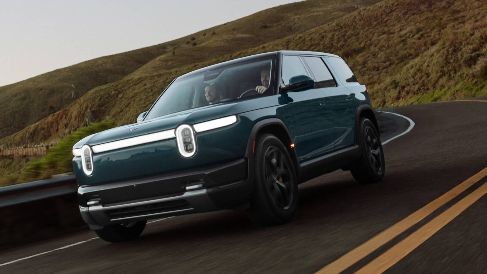 Rivian R2 in Catalina Blue driving on a coastal mountain road at dusk