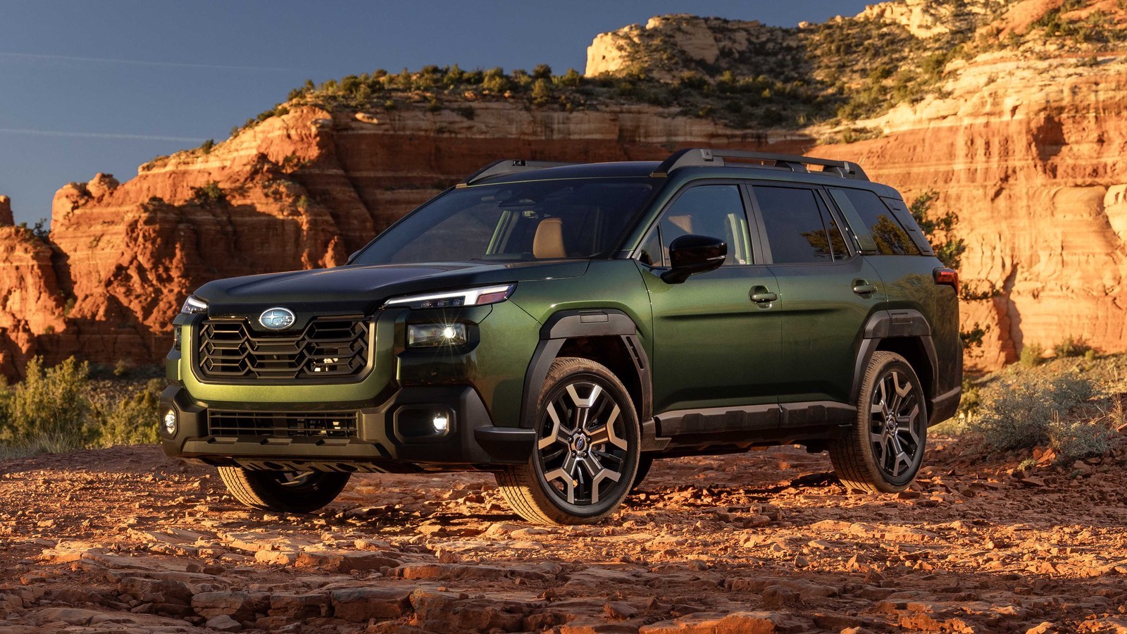 Green 2027 Subaru Outback parked on a rocky trail in front of red sandstone cliffs
