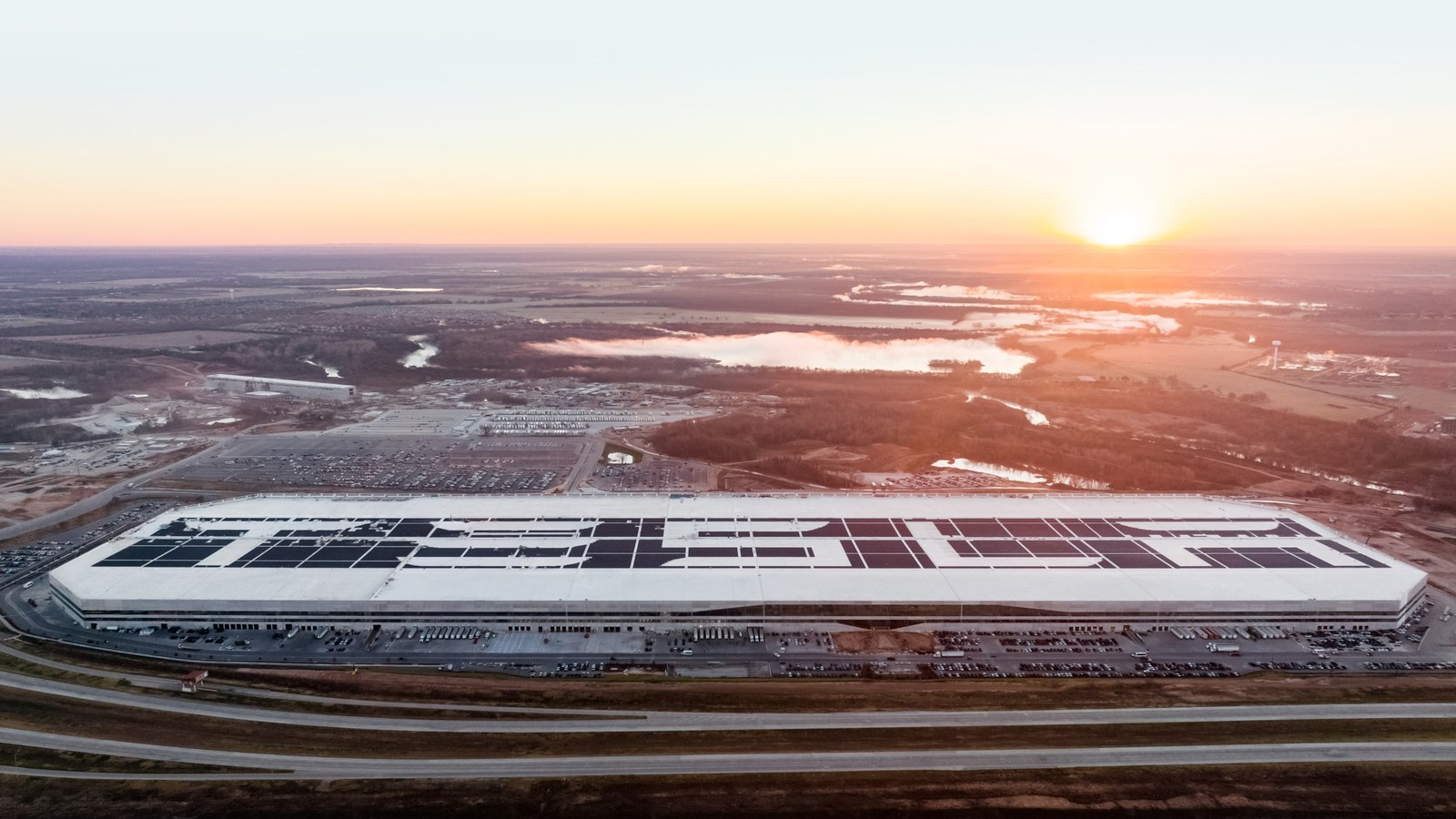 Aerial view of Tesla Gigafactory Texas at sunrise with the Tesla wordmark in rooftop solar panels