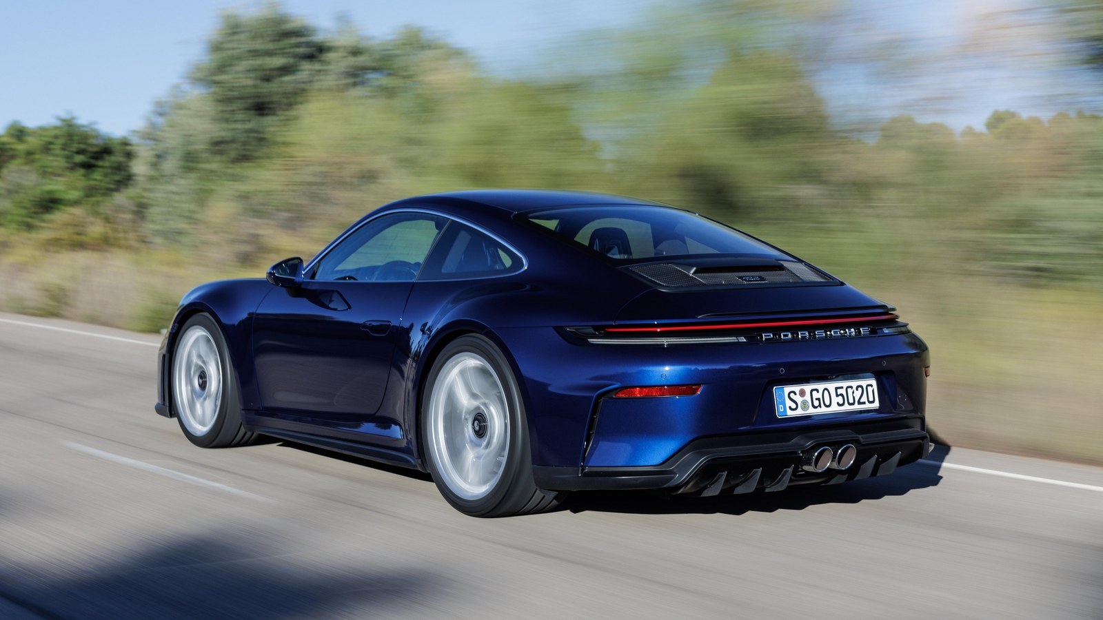 Dark blue Porsche 911 GT3 with Touring Package driving on a country road, rear three-quarter view