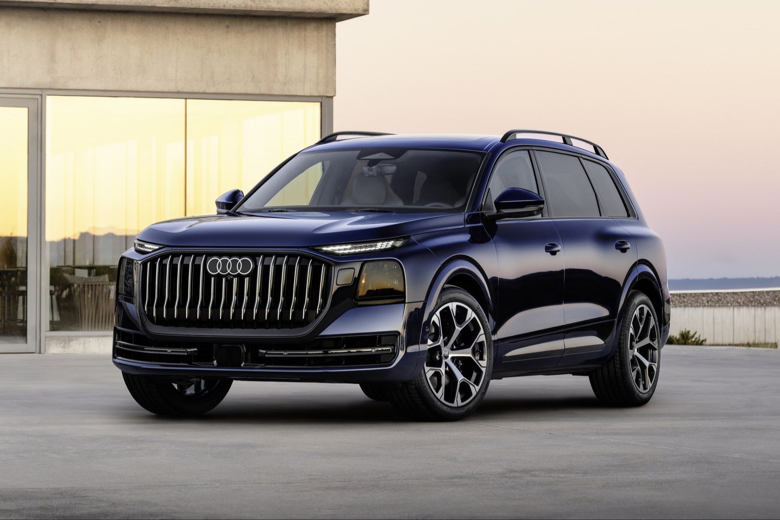 Dark blue 2027 Audi Q9 full-size SUV parked in front of a concrete building at dusk