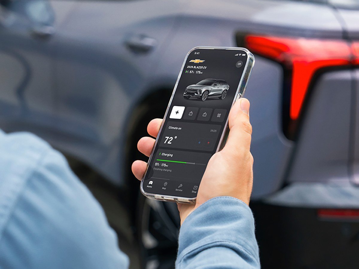Hand holding a phone with the Chevrolet mobile app open next to a vehicle