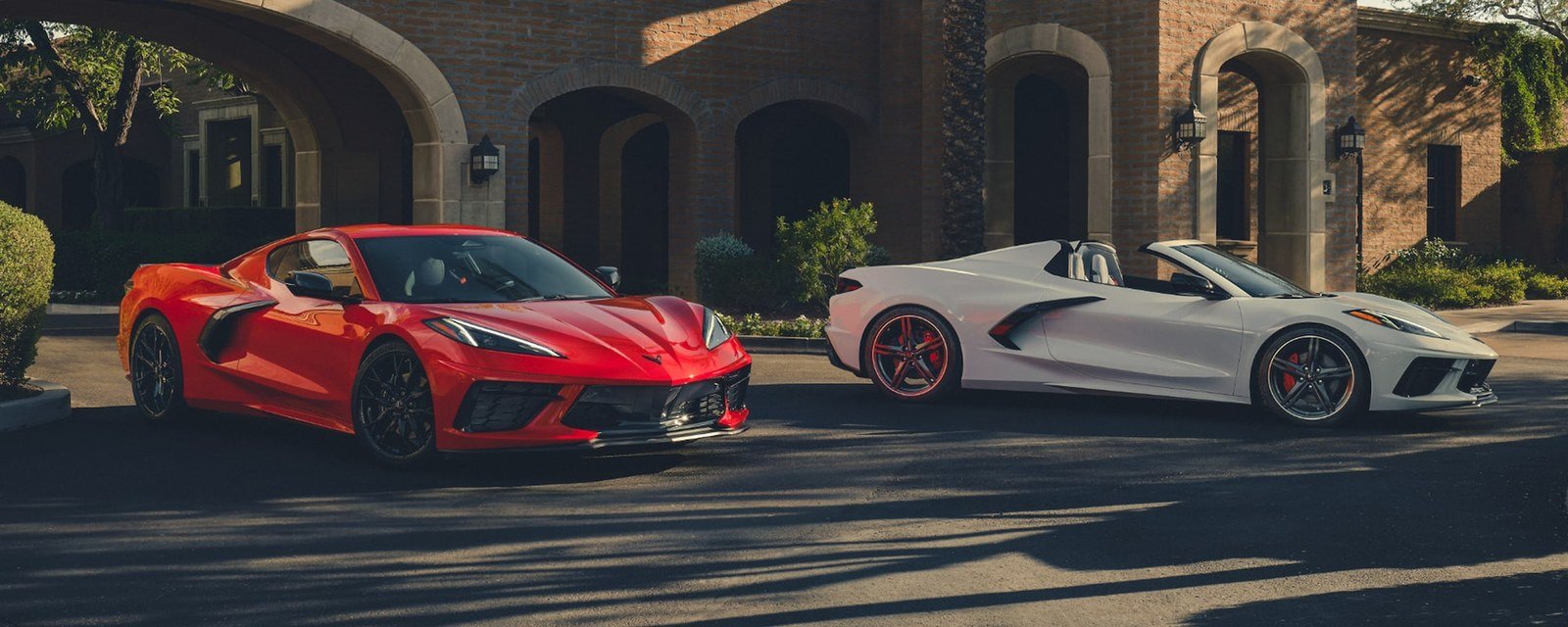 Red 2027 Corvette Stingray coupe and white convertible parked in front of a stone building