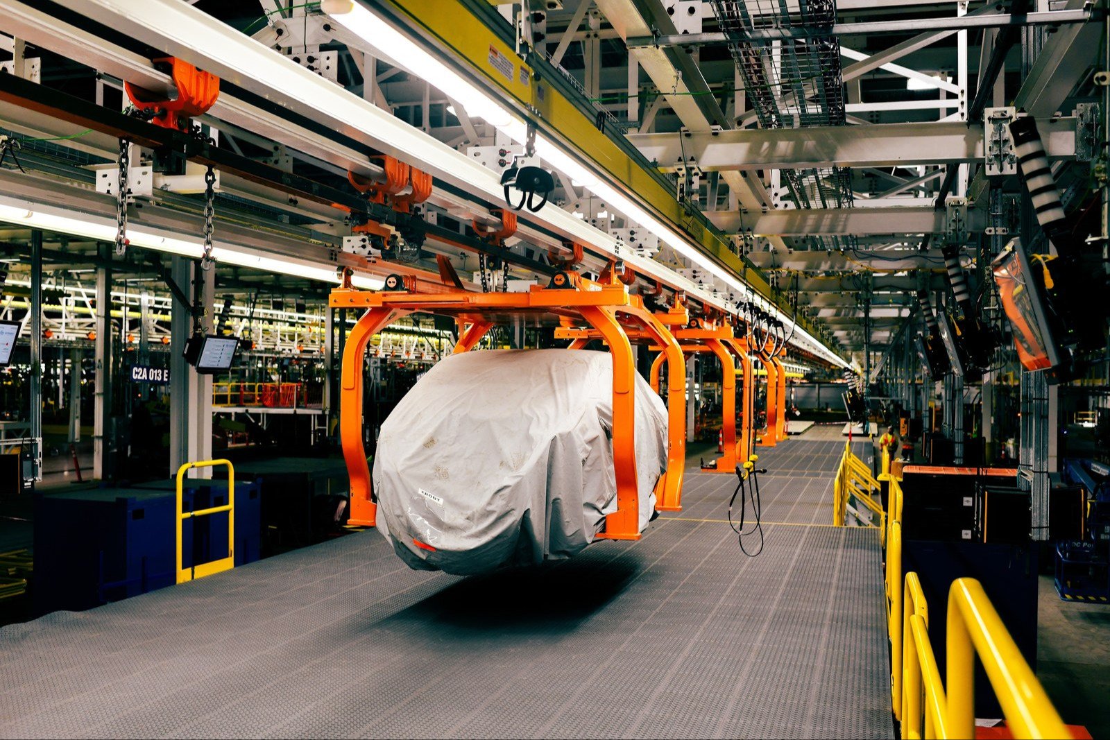 Covered vehicle hanging from an orange carrier on a Ford assembly line