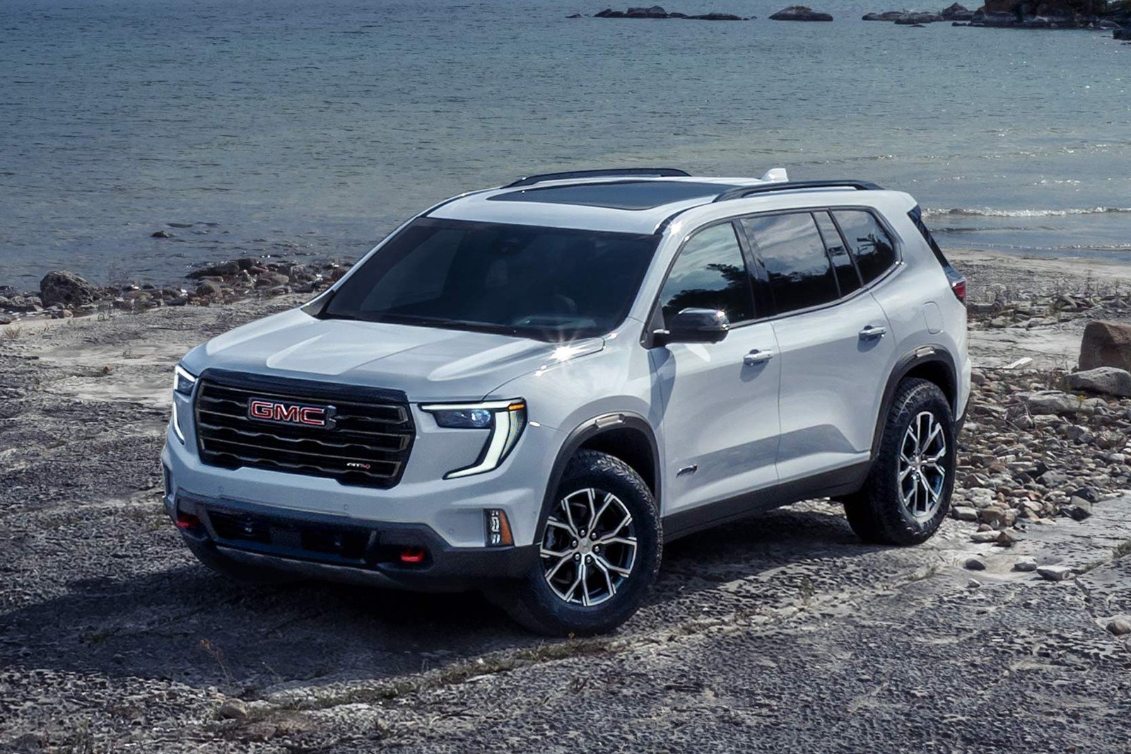 White 2027 GMC Acadia on a rocky beach, front three-quarter view