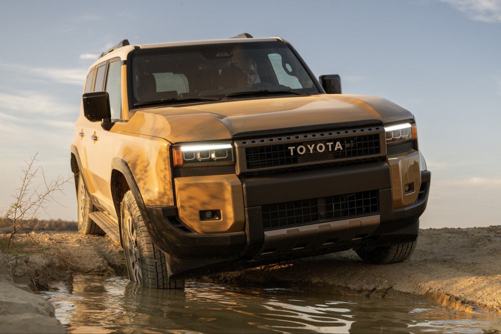 Tan Toyota Land Cruiser driving out of a shallow water crossing