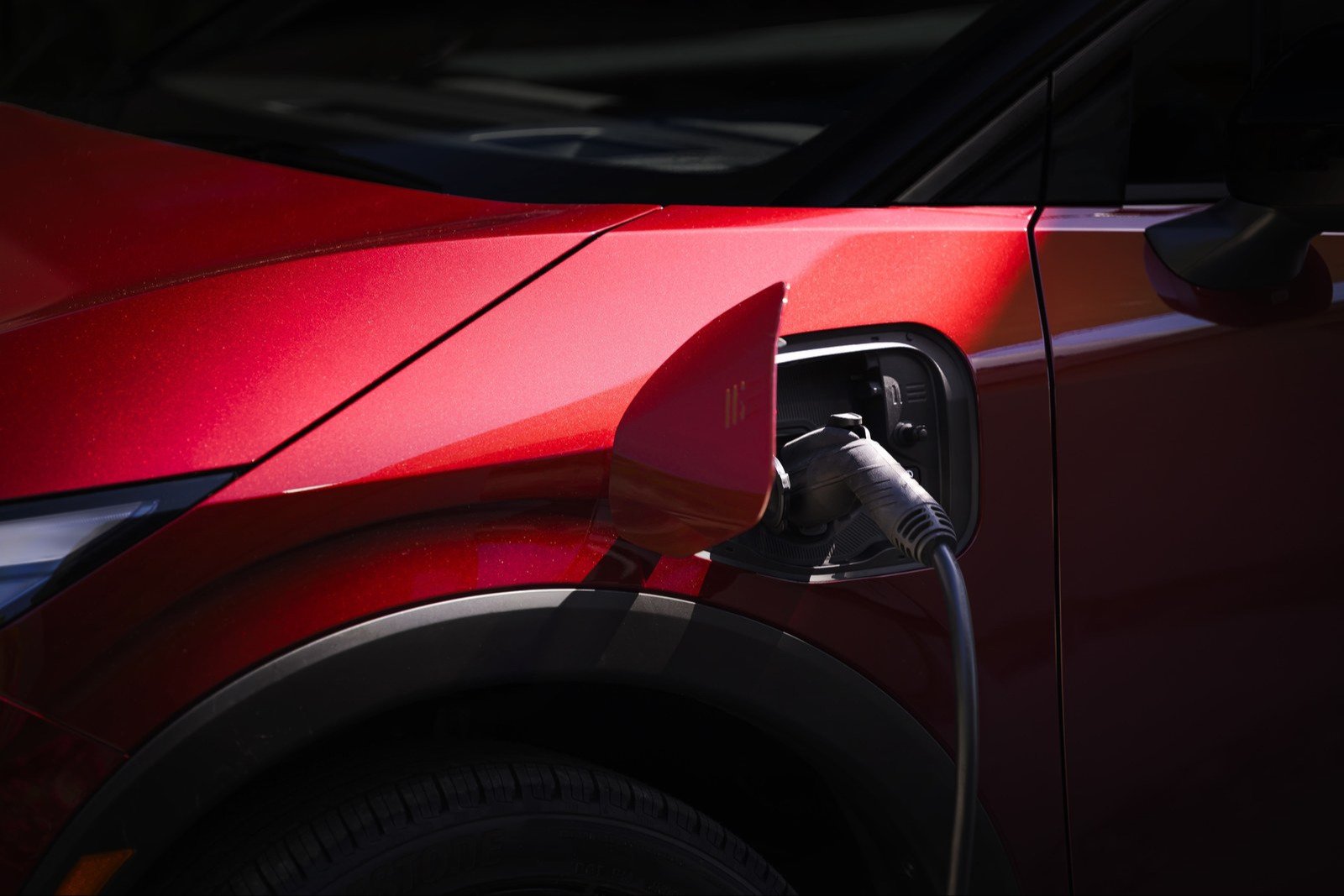 A charging connector plugged into the port of a red 2026 Nissan Leaf