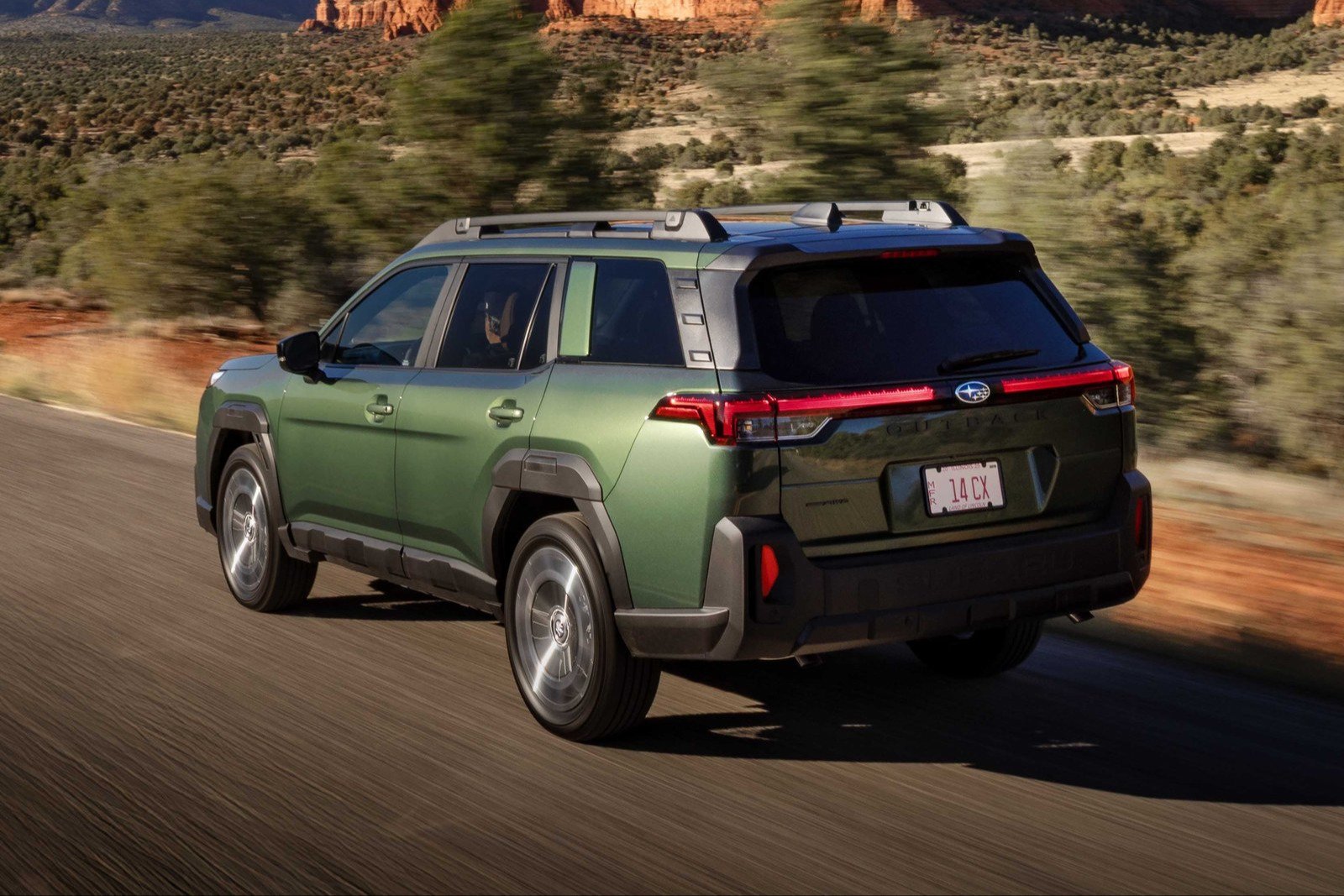 Rear three-quarter view of a green Subaru Outback driving on a desert road