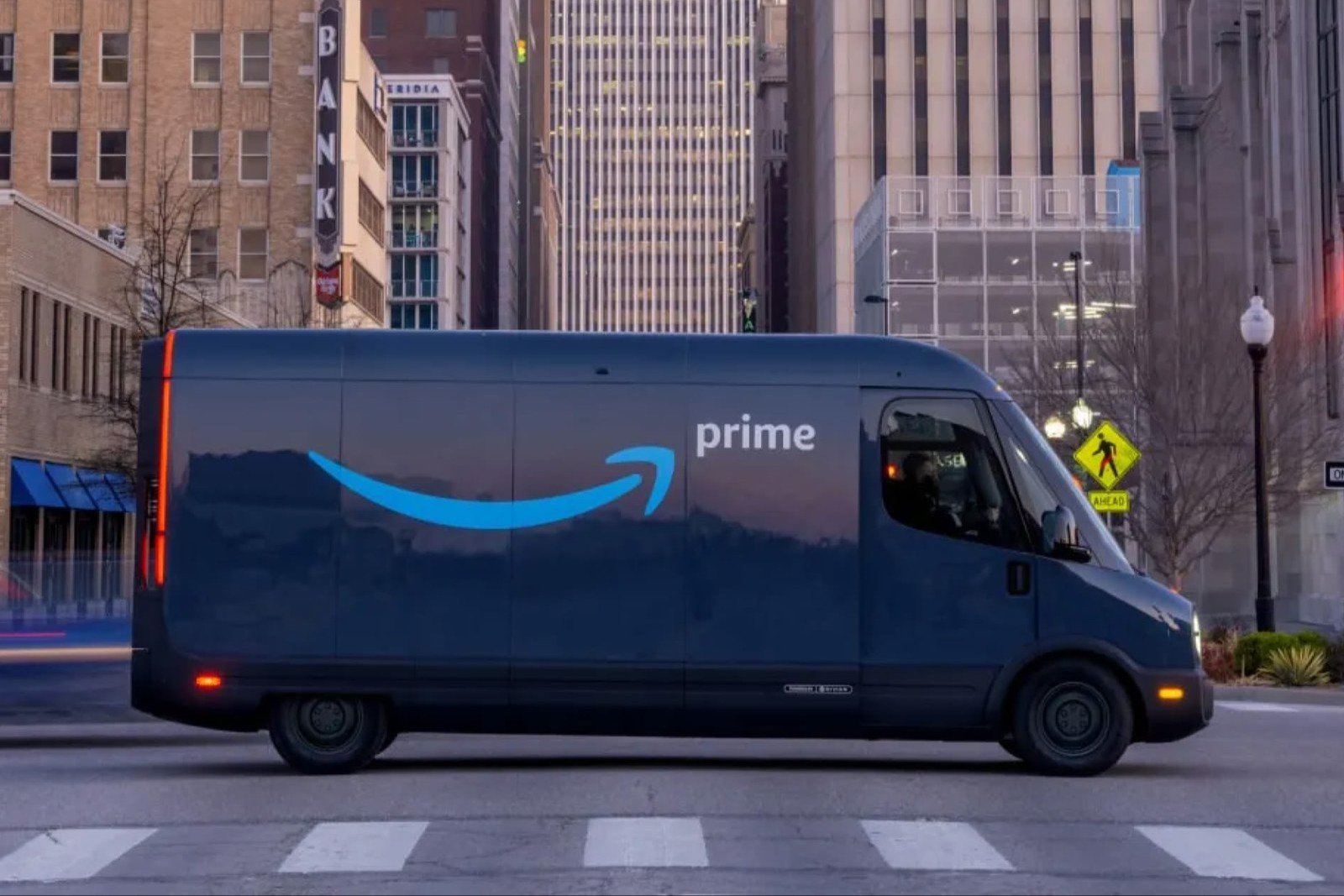 Amazon Prime-branded Rivian electric delivery van crossing a downtown intersection