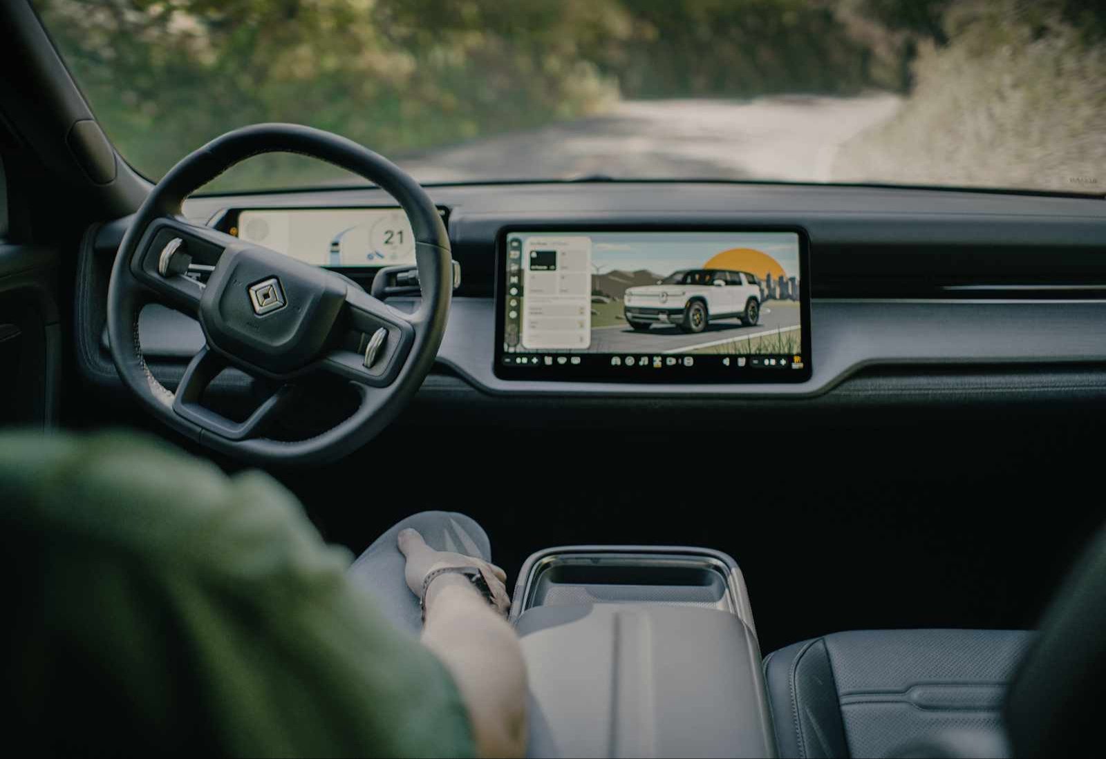 Rivian R2 cabin with the driver's hands off the wheel and the center touchscreen