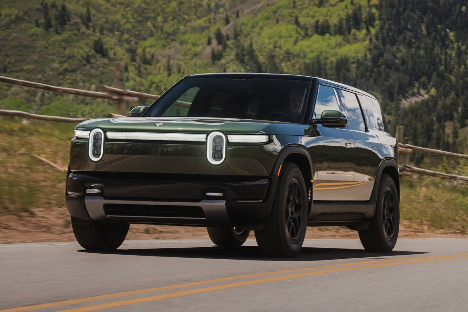 Green Rivian R2 driving on a mountain road in Utah