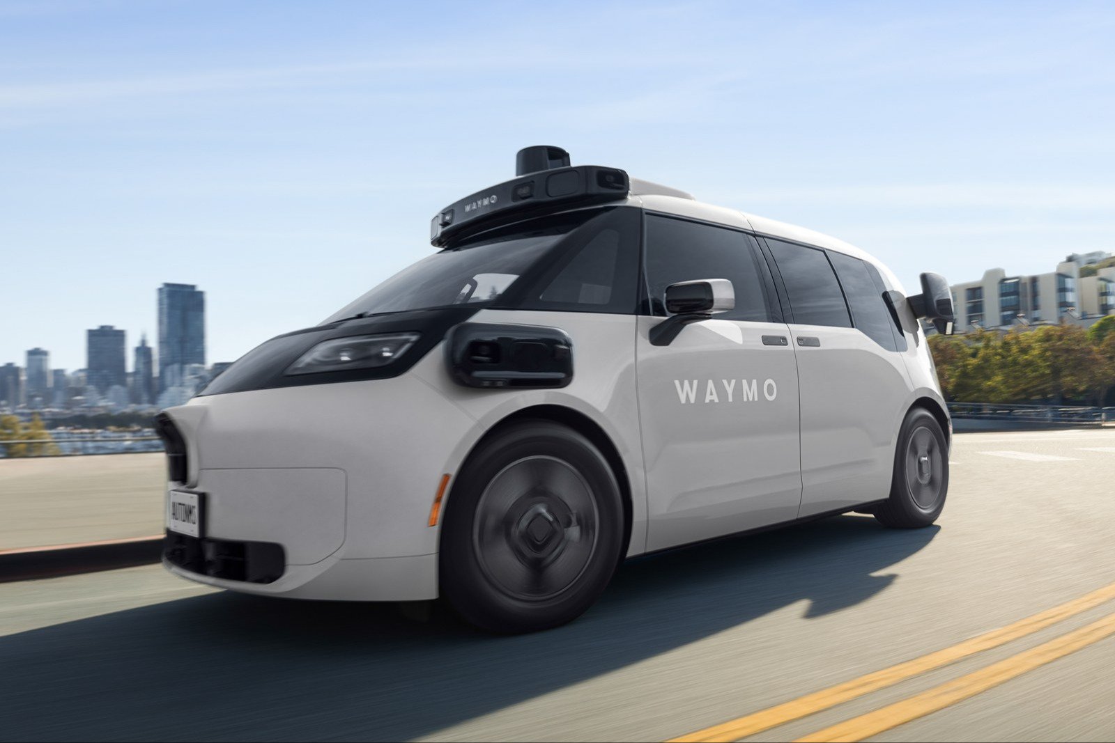 White Waymo Ojai robotaxi van built by Zeekr driving on a curving road with San Francisco skyline behind