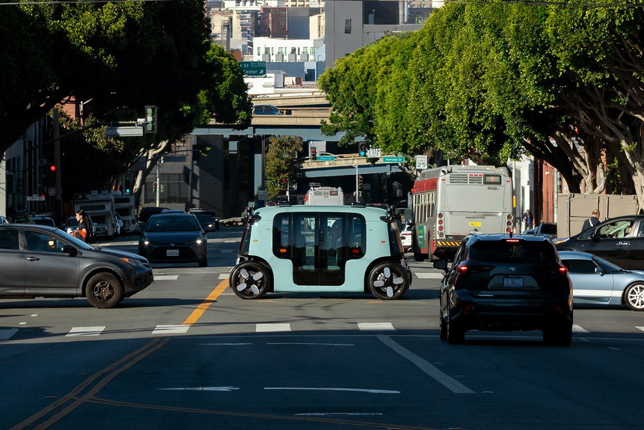 Zoox robotaxi with no steering wheel crossing a city intersection in traffic